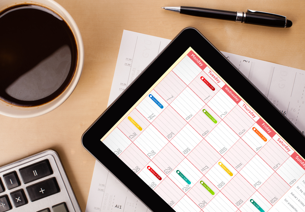 Workplace with tablet pc showing calendar and a cup of coffee on a wooden work table close-up Workplace with tablet pc showing calendar and a cup of coffee on a wooden work table close-up